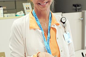 Blonde female nurse holds a small beige insulin delivery device in her palm.