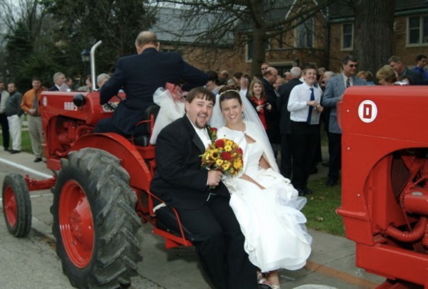 A bride and groom ride away from their wedding on the back of a red tractor