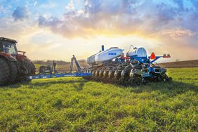 The Kinze 5670 planter in a field at sunrise, pulled by a red tractor.