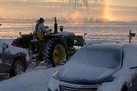 A sundog hovers on the horizon as Jerry Nelson uses his John Deere â3010â tractor to clear snow after a recent prairie blizzard.